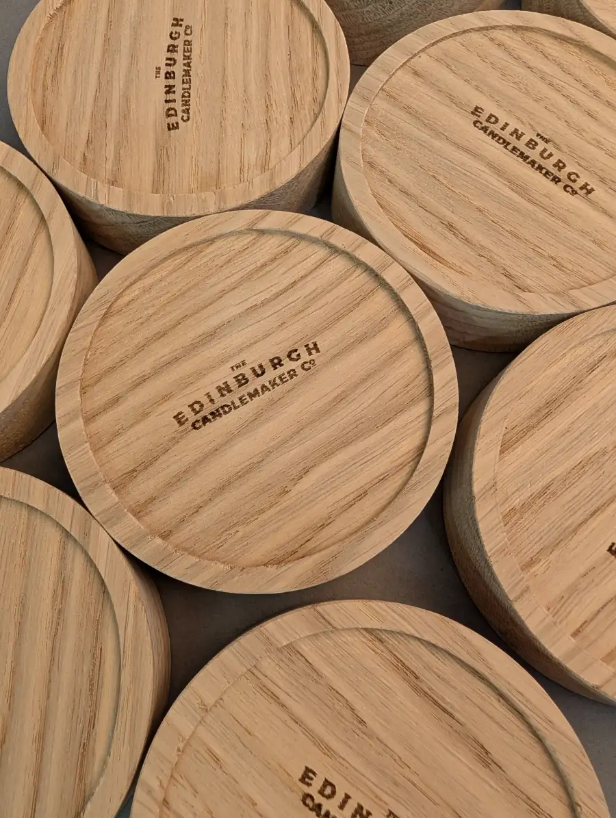 Close-up of custom laser-engraved wooden candle lids featuring The Edinburgh Candlemaker Co logo.